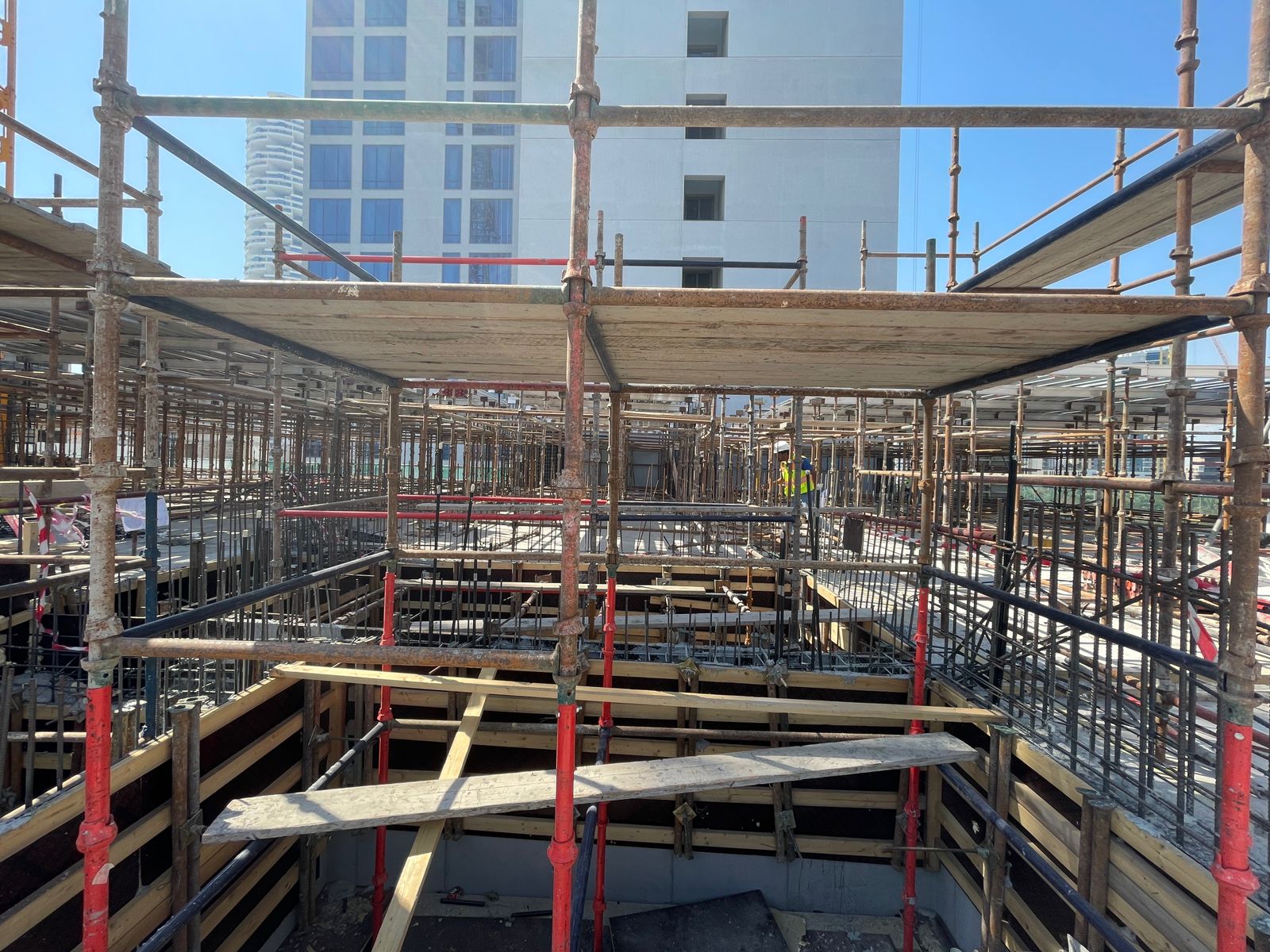 Pearl House By Imtiaz Construction site featuring scaffolding, wooden planks, and reinforcement bars, with a building partially visible above.
